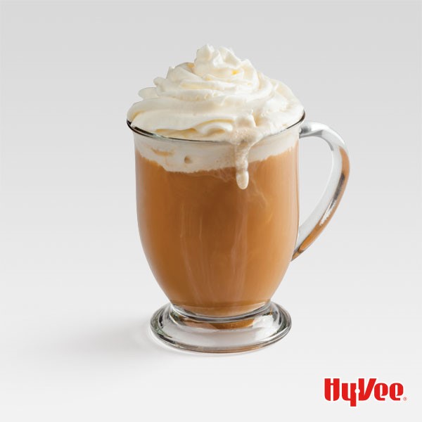 Caramel colored coffee in a glass mug with whipped topping