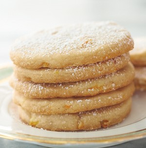 Stacked orange cookies on a gold rimmed plate and dusted with powdered sugar