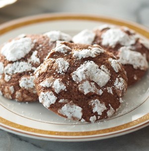 Chocolate crinkle cookies dusted with powdered sugar on a white and gold rimmed plate