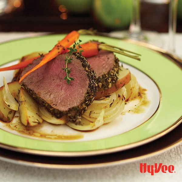 Herb-crusted beef tenderloin on top of roasted carrots, onions, and potatoes with fresh thyme for garnish