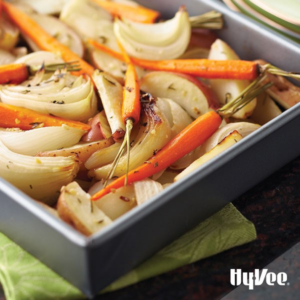Dark grey pan filled with potato and white onion wedges and whole roasted carrots