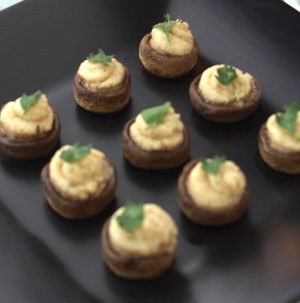 Whole filled mushrooms on a black plate topped with fresh herbs