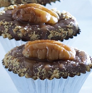 Muffin tins filled with bite-size chocolate turtle cheesecakes, topped with whole pecans