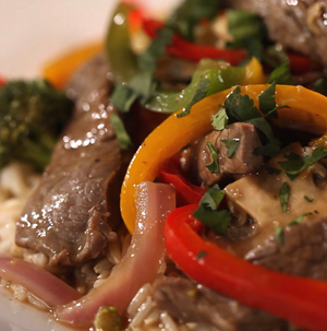Sliced sirloin steak mixed with sliced red and yellow peppers and red onions and topped with fresh herbs