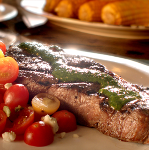 Plate of steak covered in chimichurri sauce served with cherry tomatoes