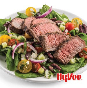 Salad topped with tomatoes, olives, red onions, and thinly cut steak