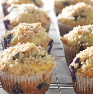 White muffin tins filled with bluberry crumb muffins on a wire rack