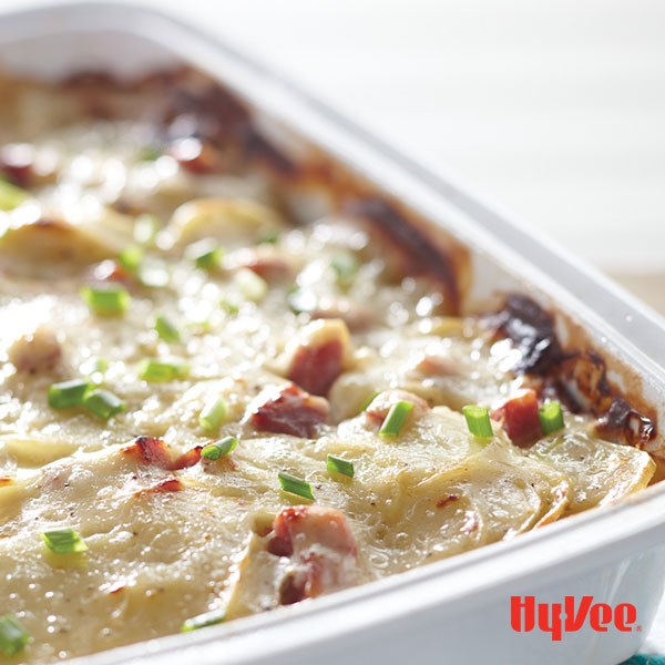 Casserole dish filled with scalloped potatoes, cubed ham, cream sauce and garnished with green onion