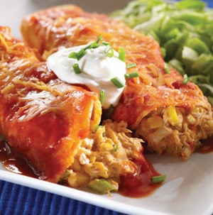 Plate of cheesy chicken enchiladas, topped with sour cream and chopped green onion