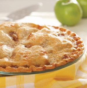 Double crusted apple pie with yellow napkin and granny smith apples in background