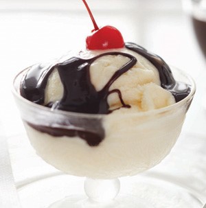 Cup of vanilla ice cream drizzled in melted chocolate and topped with a maraschino cherry