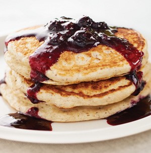 Stack of blueberry cream pancakes with blueberry sauce on a white plate