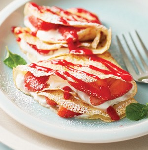 Strawberry and cream-filled crepes, topped with red raspberry sauce