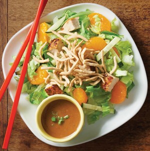 Plate of Asian chicken salad with side of dressing served on a white plate with red chopsticks