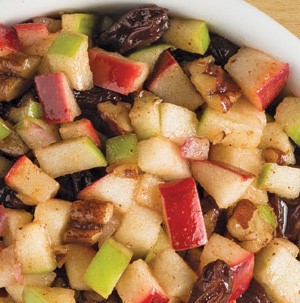 Multicolored chopped apples with skin, dried fruit, nuts and sprinkle of cinnamon in a white bowl