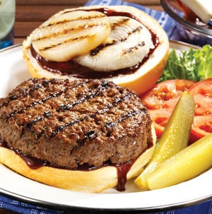 Grilled hamburger, onions and barbecue sauce sandwiched between a bun, served with pickles, lettuce and tomatoes on a white plate