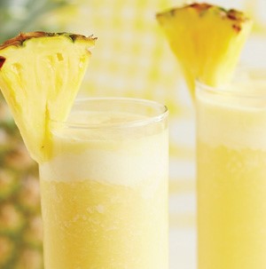 Yellow pineapple smoothies in tall glasses with pineapple wedge on rim