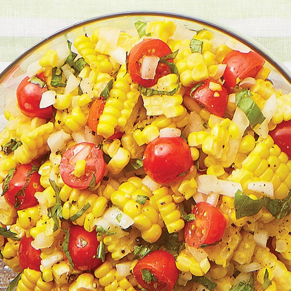 Clear bowl filled with fresh corn, halved cherry tomatoes, sliced basil, and chopped white onion