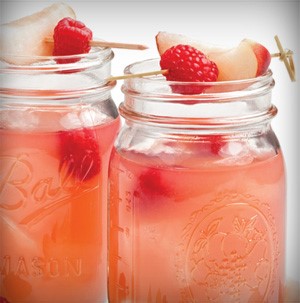 Mason jars filled with pink raspberry nectarine lemonade and topped with skewers of whole raspberries and nectarine wedge