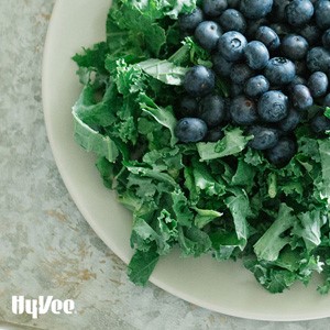 Chopped kale topped with fresh whole blueberries on a white circular plate