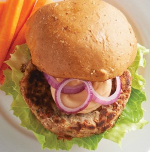 Bean burger patty with lettuce, mayo sauce and red onions sandwiched between a whole wheat bun and served with carrot sticks on a plate