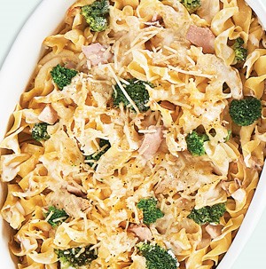 Noodles topped with tuna, broccoli florets, and melted cheese in casserole dish