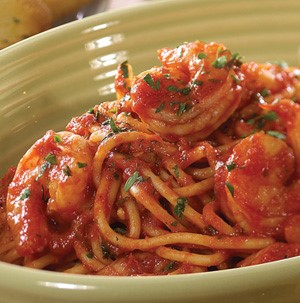 Spaghetti topped with red sauce, cooked shrimp, and finely chopped parsley in a green bowl