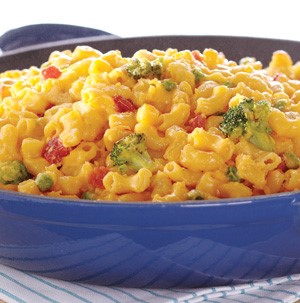 Bowl of macaroni and cheese mixed with broccoli florets, sweet peas and tomatoes