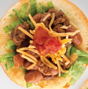 Biscuit topped with ground beef, beans, shredded lettuce, shredded cheese, and dollop of red salsa