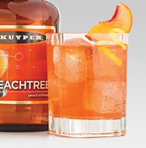 Glass filled with orange Royal Peach drink and topped with a peach slice and lemon peel