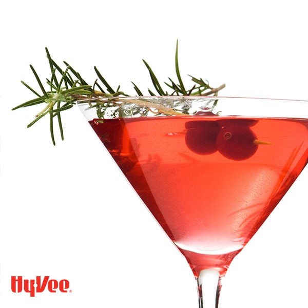 Glass of Christmas martini, garnished with rosemary and pomegranate seeds