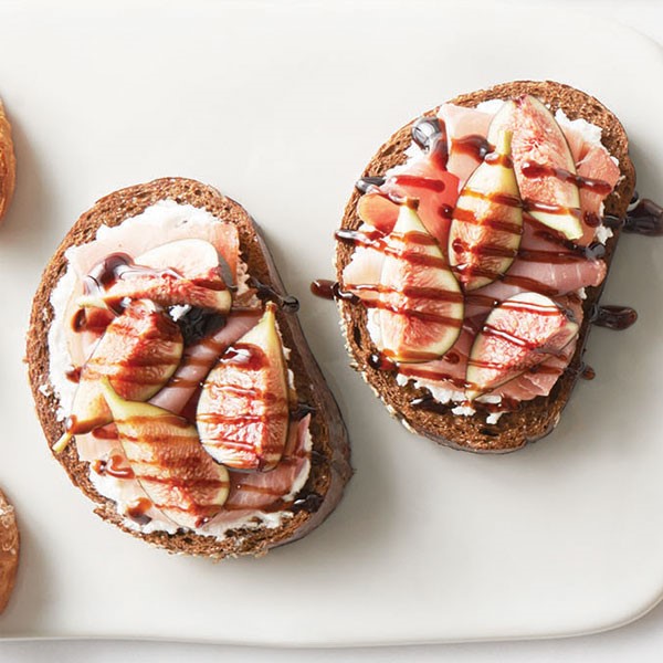 Pumpernickel bread topped with sliced prosciutto fig wedges and drizzled with balsamic glaze