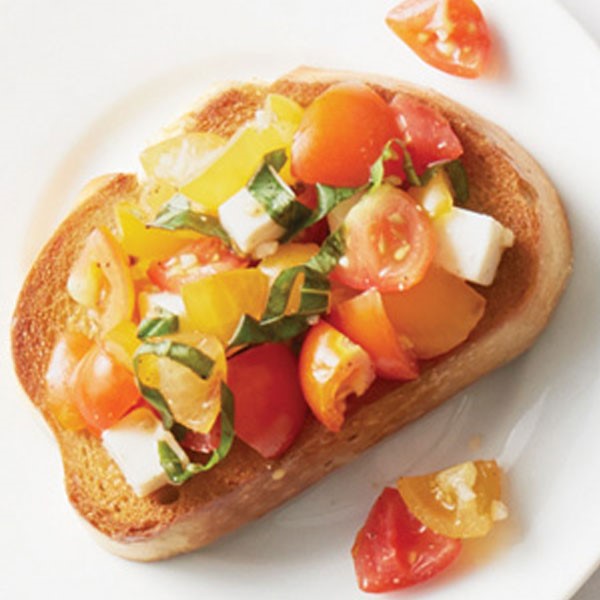 Toasted bread topped with mozzarella cubes, halved yellow and red cherry tomatoes, and fresh chopped basil