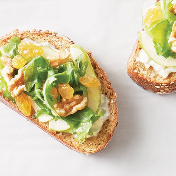 Toasted bread topped with arugula, walnuts, and golden raisins