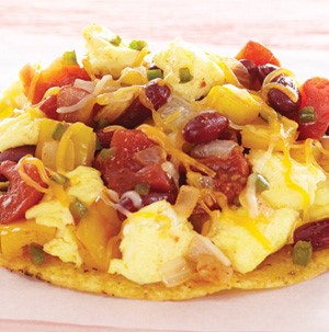 Corn tostada topped with scrambled eggs, melted cheese, kidney beans, and salsa