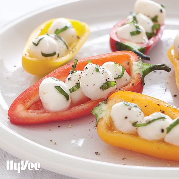 Halved mini bell peppers filled with fresh mozzarella pearls and garnished with chopped basil and black pepper