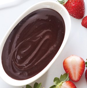 Dark chocolate sauce in white bowl surrounded by halved strawberries