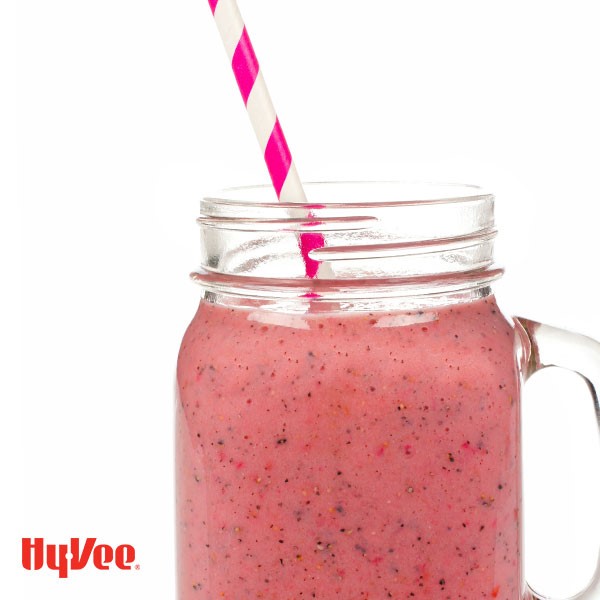 Red smoothie in a clear mason jar mug with white and pink striped straw