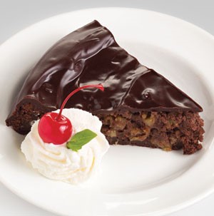 Slice of chocolate cherry cake on a white plate served with a side of whipped topping, a maraschino cherry and a mint leaf