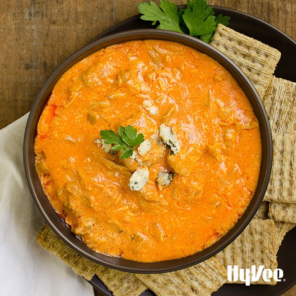 Crock pot filled with buffalo chicken dip topped with crumbled blue cheese, parsley and a side of crackers