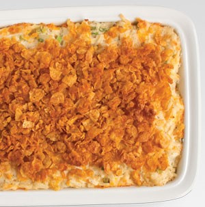 White casserole dish filled with potato casserole and flaked corn cereal on top