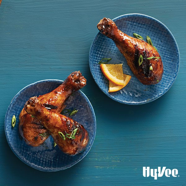 Small blue plates of chicken drumsticks covered in plum sauce and green onions