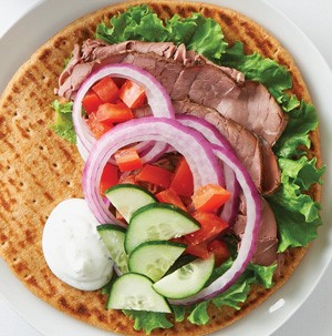 Flat pita topped with chopped tomatoes, cucumbers, sliced red onions, shaved deli meat, and lettuce leaves
