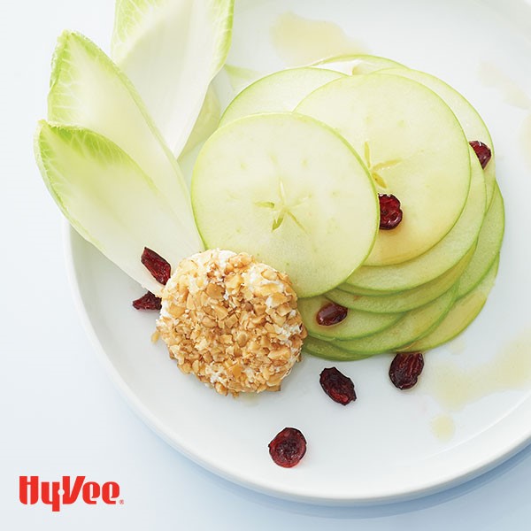Thinly sliced green apples on a plate with endive and a nut crusted goat cheese ring
