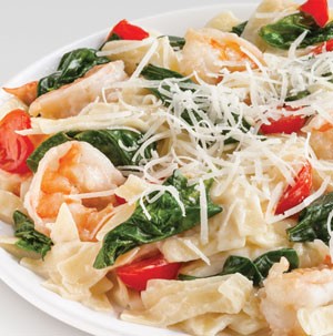 Creamy pasta and shrimp with halved cherry tomatoes, spinach, and shredded cheese