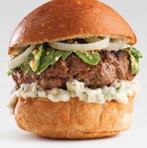 Bun topped with blue cheese spread, burger patty, greens, and yellow onions