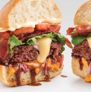 Bun topped with melted cheese, burger patty, sliced bacon, and sliced tomatoes