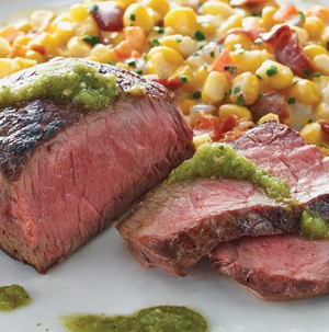 Salsa verde topped sliced steak with a side of creamed corn