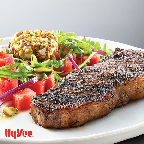 Steak with side of cubed watermelon, arugula, red onion, and cheese covered in crushed nuts