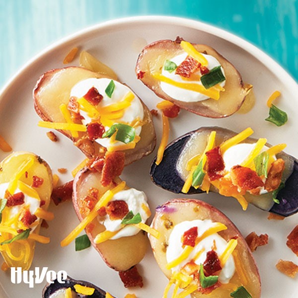 Halved yellow, red, and purple fingerling potatoes with melted cheese, chopped bacon, and chopped green onions